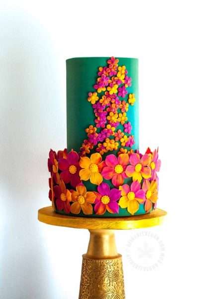 Spring teal cake with sugar flowers, sitting on a gold cake stand. Large and small flowers made with gum paste.
